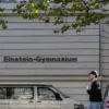 Schriftzug „Einstein-Gymnasium“ an einem Schulgebäude, davor ein Passant