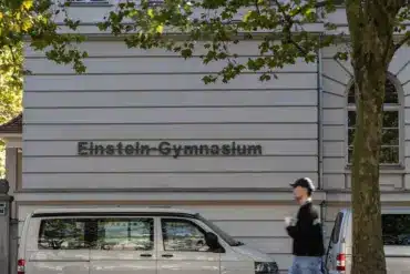 Schriftzug „Einstein-Gymnasium“ an einem Schulgebäude, davor ein Passant