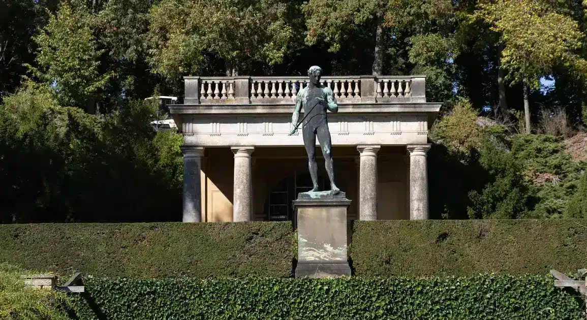 Bronzestatue vor einem klassizistischen Pavillon in einer Parkanlage