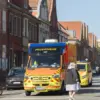 Rettungswagen der Feuerwehr fährt durch eine Straße mit Backsteinhäusern, daneben Radfahrer