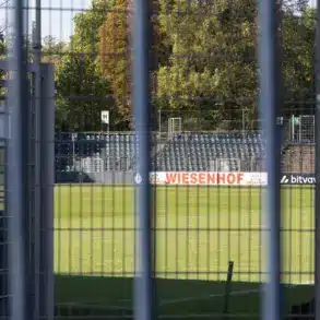Blick durch einen Gitterzaun auf Rasen und Tribüne des Karl-Liebknecht-Stadions