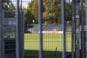 Blick durch einen Gitterzaun auf Rasen und Tribüne des Karl-Liebknecht-Stadions