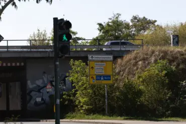 Fußgängerampel vor einer Bahnunterführung mit gelbem Wegweiser