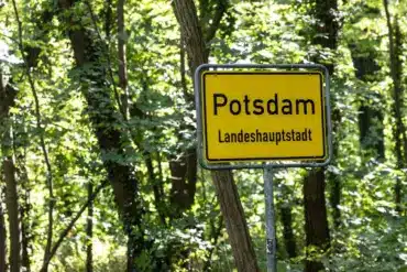 Gelbes Ortsschild „Potsdam Landeshauptstadt“ vor Bäumen