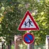 Verkehrsschild „Achtung Kinder“ über einem Halteverbotsschild vor einem Zaun
