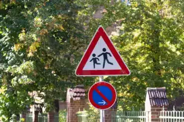 Verkehrsschild „Achtung Kinder“ über einem Halteverbotsschild vor einem Zaun
