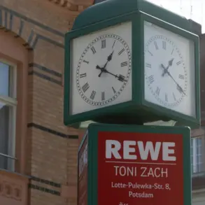 Straßenuhr über einem REWE-Schild mit Adresse und Öffnungszeiten vor Altbauten