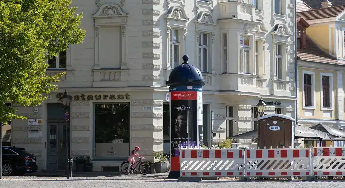 Litfaßsäule und Baustellenabsperrung vor einem Altbau mit Restaurant