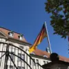 Deutschland- und Brandenburg-Flagge vor einem historischen Regierungsgebäude hinter einem Eisentor