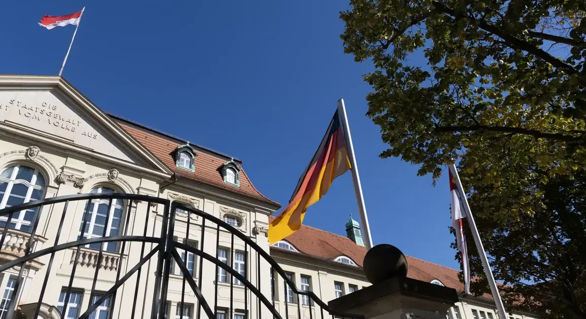Deutschland- und Brandenburg-Flagge vor einem historischen Regierungsgebäude hinter einem Eisentor