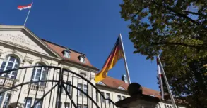 Deutschland- und Brandenburg-Flagge vor einem historischen Regierungsgebäude hinter einem Eisentor