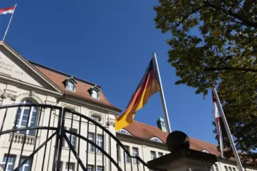 Deutschland- und Brandenburg-Flagge vor einem historischen Regierungsgebäude hinter einem Eisentor