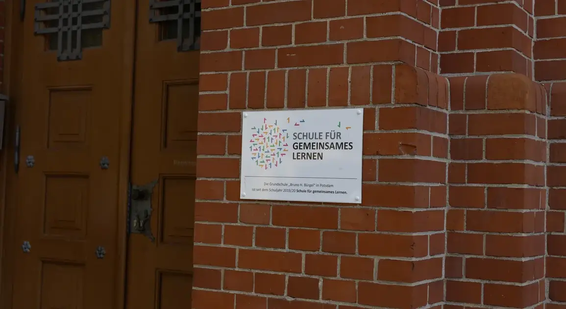 Schild „Schule für gemeinsames Lernen“ neben der Holztür einer Grundschule