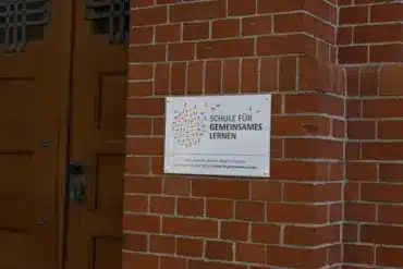 Schild „Schule für gemeinsames Lernen“ neben der Holztür einer Grundschule