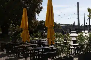 Leerer Biergarten mit Holztischen und geschlossenen gelben Sonnenschirmen