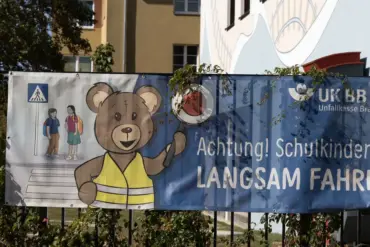 Banner der Unfallkasse Brandenburg „Achtung! Schulkinder! Langsam fahren“ an einem Zaun