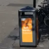 Orangefarbener Self-Service-Mülleimer der Stadtreinigung, dahinter abgestellte Fahrräder