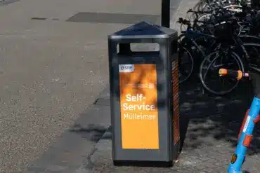 Orangefarbener Self-Service-Mülleimer der Stadtreinigung, dahinter abgestellte Fahrräder